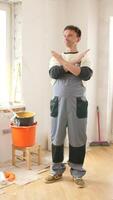 Vertical a painter is making a stop sign with his hands while standing in a room undergoing renovation, surrounded by painting tools and materials video