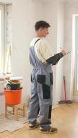 A man in overalls standing in a room with a clipboard video