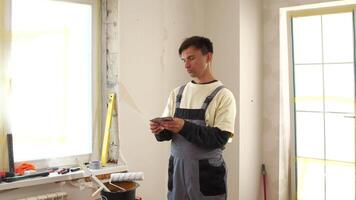A man in overalls standing in a room with a cell phone video