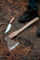 An Axe And A Knife Lie On Pine Needles Next To A Person's Boot. photo
