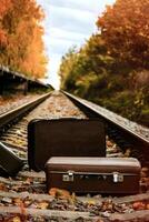 Brown vintage suitcases lying on railway tracks surrounded by autumn leaves, captured during golden hour with soft natural lighting. photo