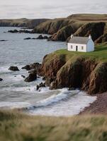 Secluded Coastal Cottage on a Dramatic Cliffside. A tranquil scene of a white house perched atop rugged cliffs overlooking a churning ocean. photo