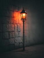 Illuminated Street Lamp Against a Stone Wall at Night. A solitary lamp casts a warm glow on a dark, textured stone wall, creating a moody and atmospheric scene. photo