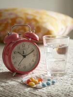 Morning Routine With Bedside Alarm Clock, Glass of Water, and Medication on Soft Bed Linens photo