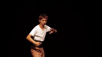 A dancer performing on stage, showcasing traditional movements in a cultural attire. The background is dark, highlighting the dancer's expressive gestures and costume. video