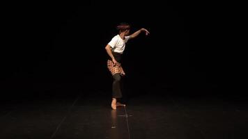 A dancer performing on stage with a dramatic pose, wearing traditional attire. The background is dark, emphasizing the dancer's movements and expression. video