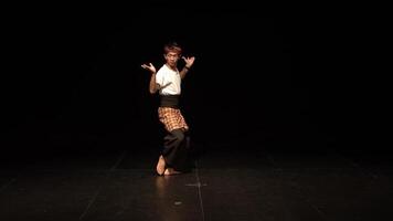 A dancer performing on stage with a dramatic pose, showcasing traditional attire and expressive movements. The background is dark, emphasizing the dancer's form and technique. video