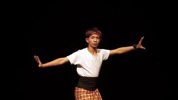 A dancer performing on stage with dramatic lighting, showcasing traditional attire and expressive movements. The background is dark, emphasizing the dancer's pose and costume. video