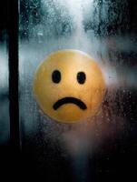 Melancholic Sick Face Drawn on Steamed Glass Window With Moody Tones Revealing a Somber Atmosphere and Empty Space photo