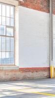 Architectural study of an industrial building's interior, featuring a large gridded window, white-painted brick wall, and sunlit concrete floor. photo