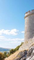 Ancient stone tower standing tall on a sun-drenched hill, overlooking a vast landscape under a clear blue sky with fluffy clouds. A historic architectural marvel. photo