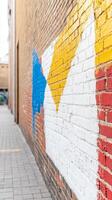 Vibrant Abstract Mural on a Textured Brick Wall in an Urban Alleyway, Featuring Bold Yellow, Blue, and White Geometric Shapes. photo