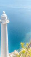 Majestic White Lighthouse Overlooking a Serene Azure Sea. Coastal Landmark Guiding Ships, Bathed in Bright Sunlight, a Symbol of Hope and Tranquility. photo
