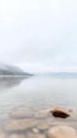 Misty Lake Serenity Tranquil Waters Reflecting Fog-Kissed Mountains and Clear Rocky Shoreline. A Peaceful Natural Landscape Vista. photo