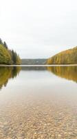 Captivating Autumn Lake Landscape Crystal Clear Water Revealing Riverbed Pebbles, Framed by Vibrant Forest Reflections photo