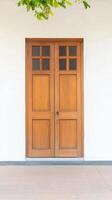 Elegant Wooden Double Door with Glass Panels Against a Pristine White Wall, Crowned by Lush Green Foliage, Evoking Serene Architectural Beauty photo