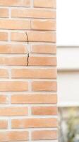 Detailed close-up of a significant vertical crack in a weathered orange brick wall, highlighting structural damage and the urgent need for building maintenance and repair photo