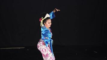 A dancer performing in traditional attire, showcasing vibrant colors and intricate patterns. The background is dark, emphasizing the dancer's movements and costume details. video