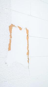 Abstract peeling white paint on a weathered concrete block wall, revealing rustic brown textures. A detailed close-up of urban decay and aged architectural surface. photo