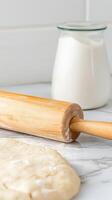 Close-up of a wooden rolling pin and fresh dough on a marble surface, with a jar of milk, perfect for homemade baking creations. photo