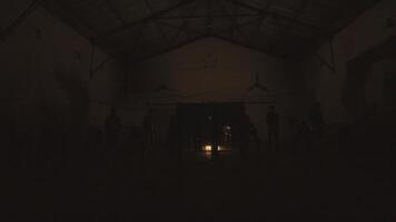 Silhouettes of people in a dark, dimly lit warehouse with a single light source in the background during the night video