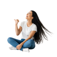 A cheerful young woman with long black hair is sitting crosslegged and pointing upwards, isolated on transparent background png