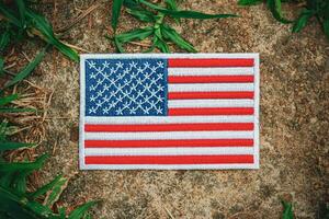 Sustainable themed US flag embroidered with thread and fabric, resting on an ancient stone bordered by fresh green grass. A calm and patriotic environmental concept. photo
