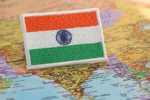 Horizontal eco-themed image of India fabric flag, hand-embroidered with traditional colors, resting on a world map at India location. Represents sustainability, travel, and green values. photo