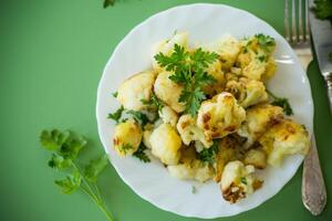 delicious dinner.Fried cauliflower with spices and herbs on a green background . photo