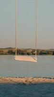 Loneliness and loneliness concept. A lonely teddy bear is riding on a swing. Two swings, on one of them sits a teddy bear against the background of a lake. video