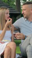 Young people are sitting on a bench and eating fruit. The girl does not let her husband eat. video