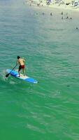 Aerial view A man learns to swim on a Sap board near a sandy shore. The man stands unsteadily on the sap board. video