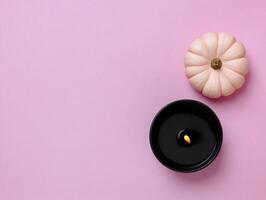 Halloween flat lay with black candle and tiny pumpkin on pink background for festive decoration photo