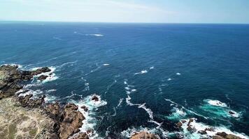 Breathtaking aerial footage of the ocean waves crashing against rocky shores under a clear blue sky. photo