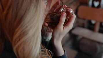Over shoulder shot. blonde woman experiencing moment of serenity while drinking herbal tea, savoring calm and warmth in soft slow motion indoor setting. Woman sipps herbal tea. Herbal Wellness Concept video