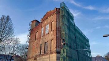 A historic brick building undergoing renovation, covered with green scaffolding, showcasing construction work. photo