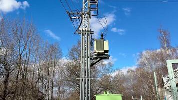 A utility pole, adorned with a transformer, stands prominently surrounded by trees under a clear blue sky above photo