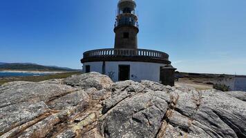 A picturesque lighthouse stands proudly among rocky terrain and calm waters beneath a bright blue sky photo