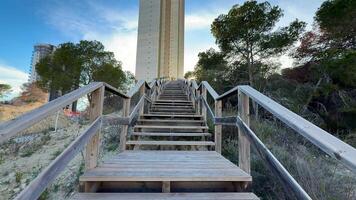 A beautifully crafted wooden staircase gracefully ascends towards a tall and impressive tower, surrounded by lush trees photo