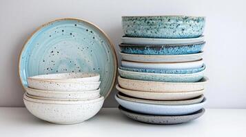 stack of ceramic plates and bowls with speckled designs in neutral and blue tones photo