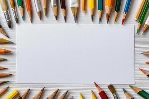 Colorful pencils and brushes frame blank white paper on wooden surface photo