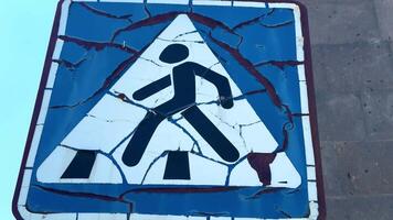 Old crosswalk with cracked paint. A sign with a person walking on it is broken video