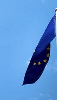 A large European flag flutters in the wind against a blue sky and a white flagpole. European Union, immigrants in Europe, asylum, for news, for newspapers. High 4k video