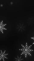 Bright glowing snowflakes on a dark black background with radial light streaks and winter ambiance video