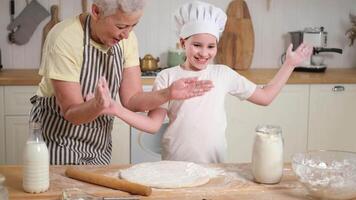 Happy family in kitchen. Kid girl grandma have fun playing clap hands with flour cooks bake cookies. Grandmother granddaughter child knead dough in kitchen. Teamwork helping family generations video