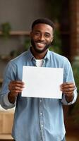 Smiling Man Holds Blank Paper in Bright Indoor Setting With Plants Around Him. photo