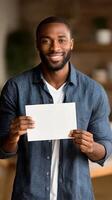 Smiling Man Holds Blank Paper in Cozy Indoor Setting During Daytime photo