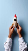 Creative Hands Holding a Wooden Toy Rocket on a Blue Background During a Playful Moment. photo