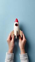 Creative Hands Holding a Wooden Toy Rocket on Blue Background During a Playful Moment photo