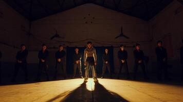A group of people standing in a dimly lit hall with a spotlight on the person in the center video